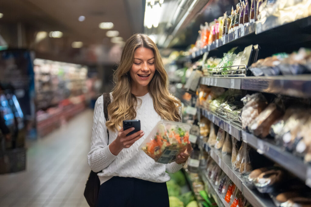 Woman checking her phone while shopping in a grocery store aisle